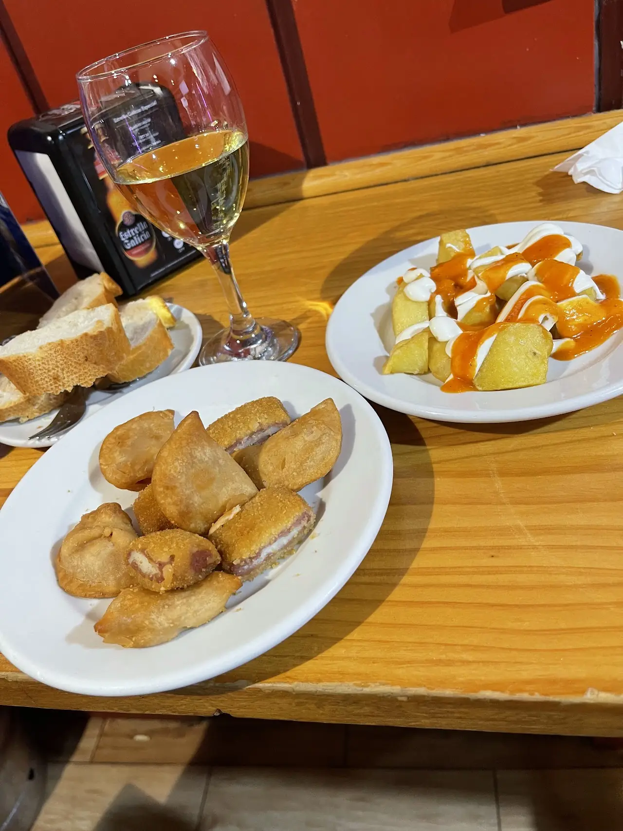 Patatas bravas with a creamy sauce and a plate of fried bites, with bread and a glass of white wine