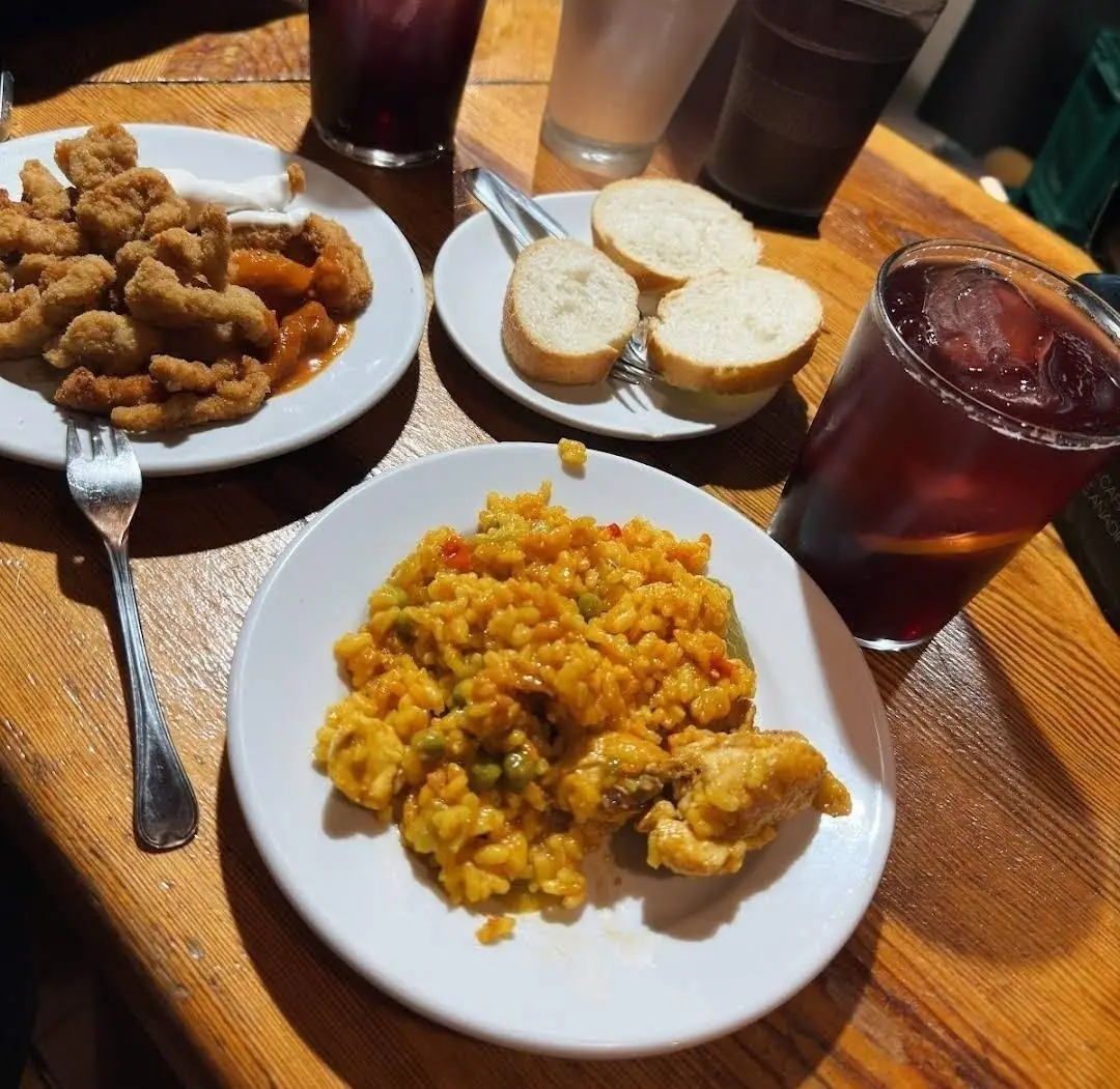 A plate of yellow rice, a plate of fried bites and bread, with glasses of tinto de verano