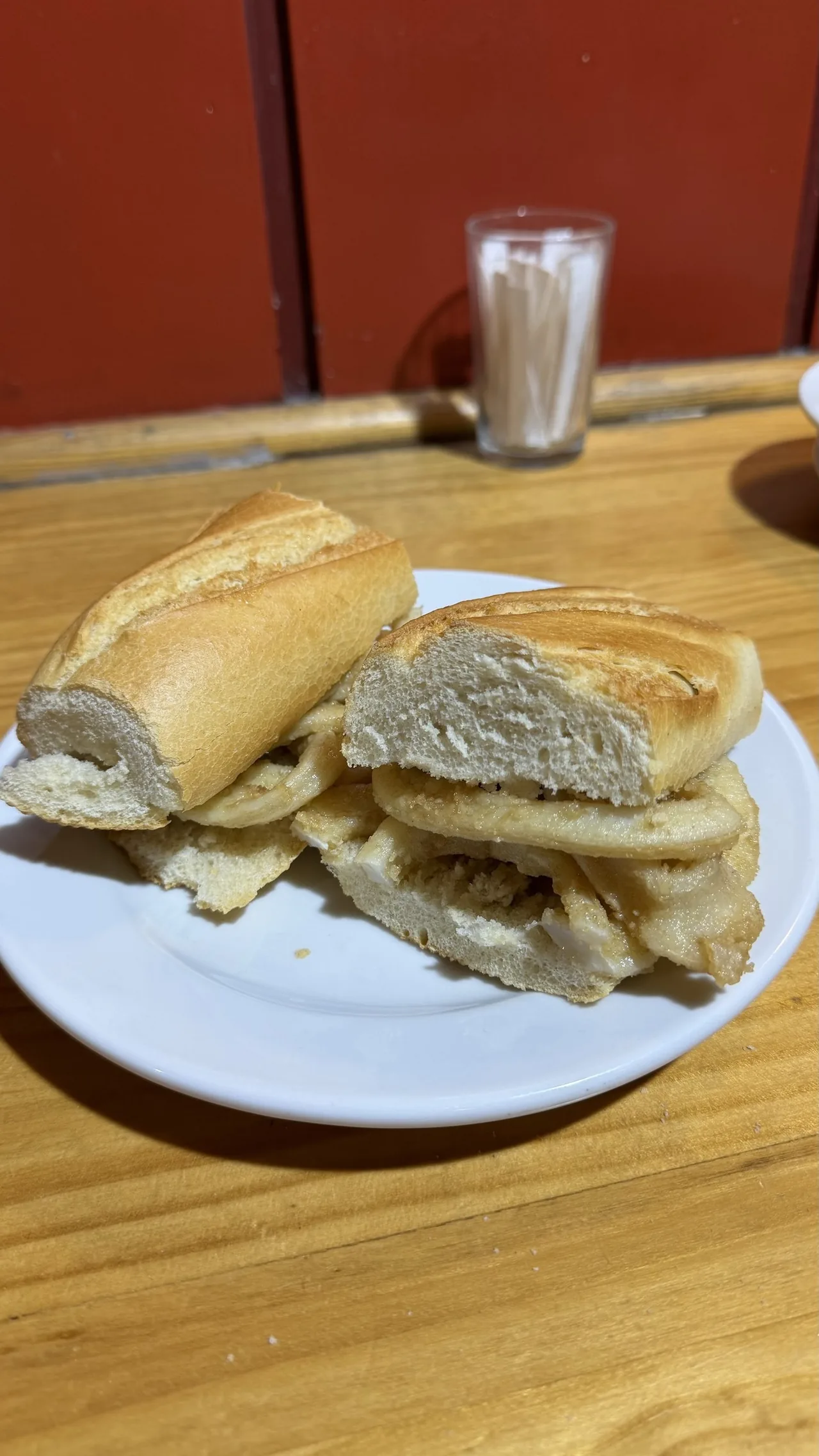 A sandwich of fried squid strips in a crusty roll on a white plate
