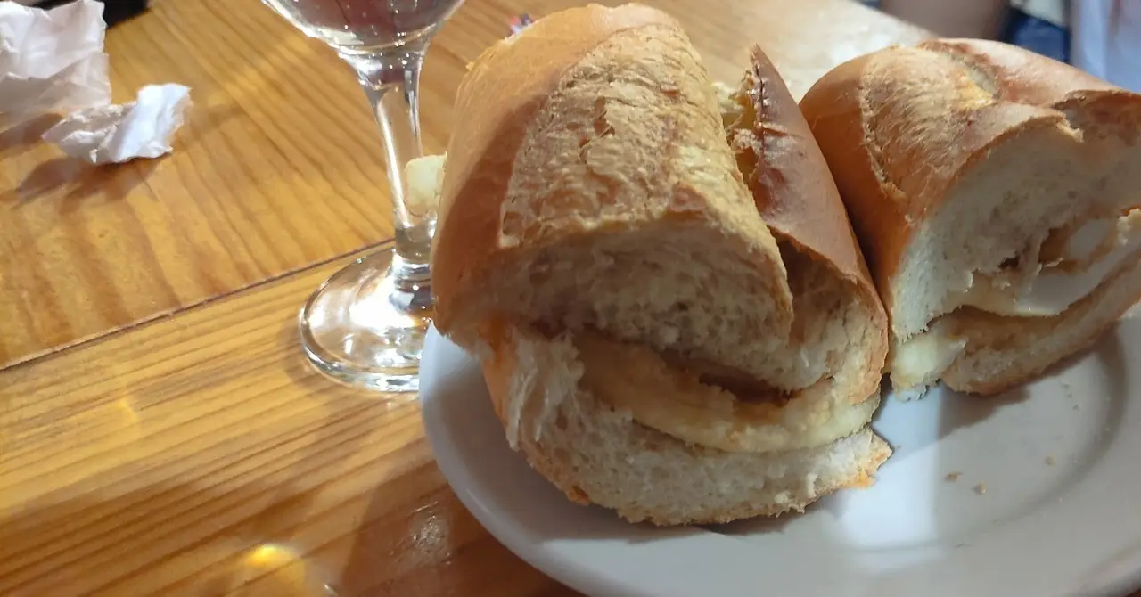 A bocadillo de calamares cut in half on a white plate on a wooden bar
