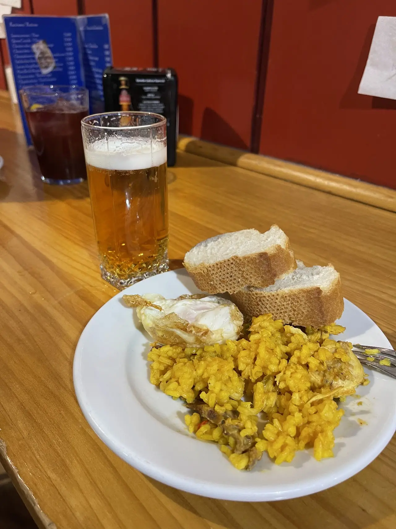A tapa of yellow rice topped with a fried egg, with bread and a glass of beer