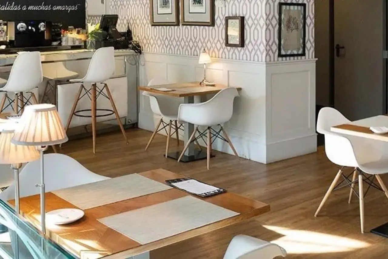 Bright cafe dining room with white Eames-style chairs, small wooden tables with placemats, table lamps and a bar counter