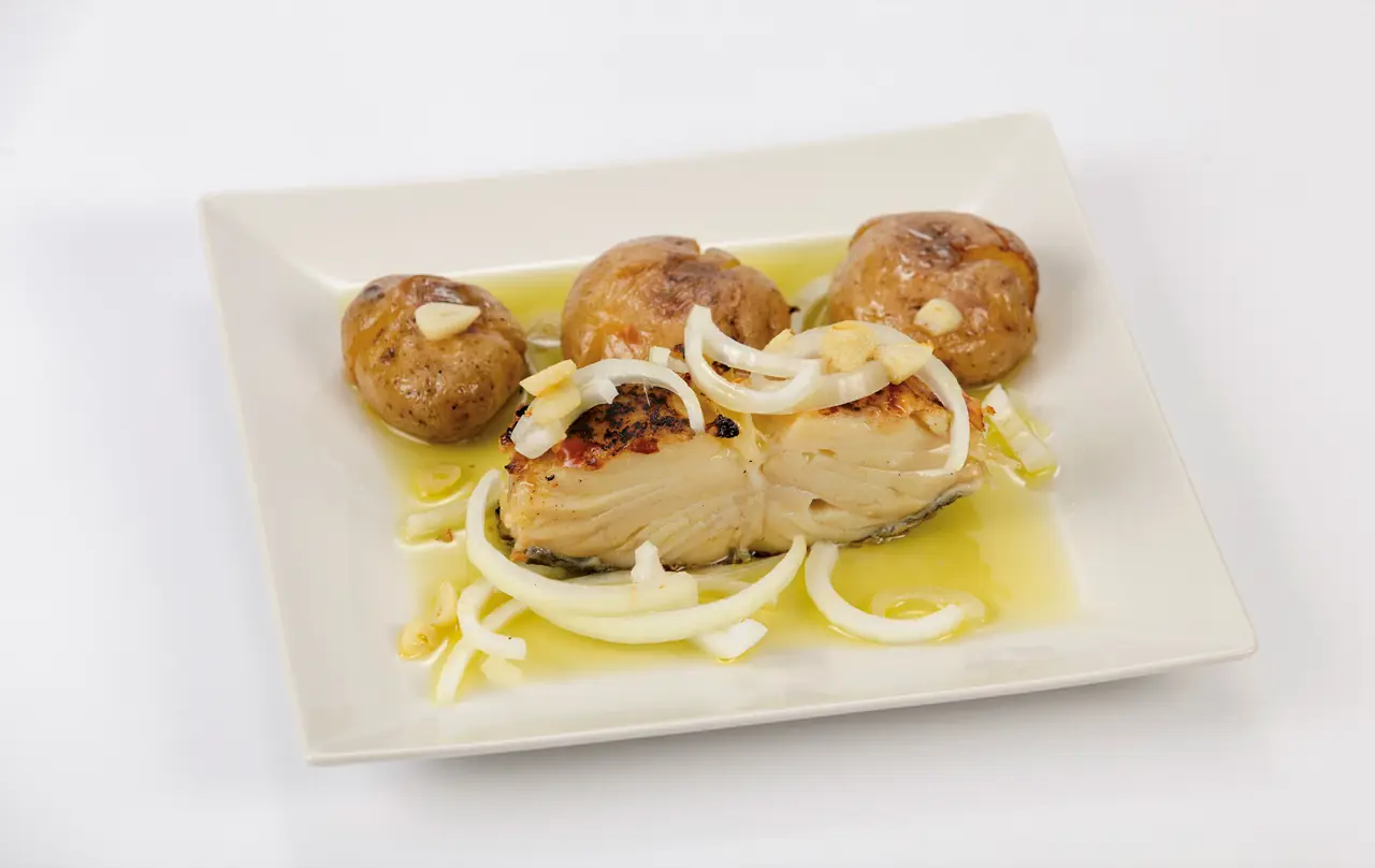 Roasted bacalao (cod) fillet with garlic slices and raw onion strips, plated with roasted baby potatoes in olive oil, at El Rey del Bacalao