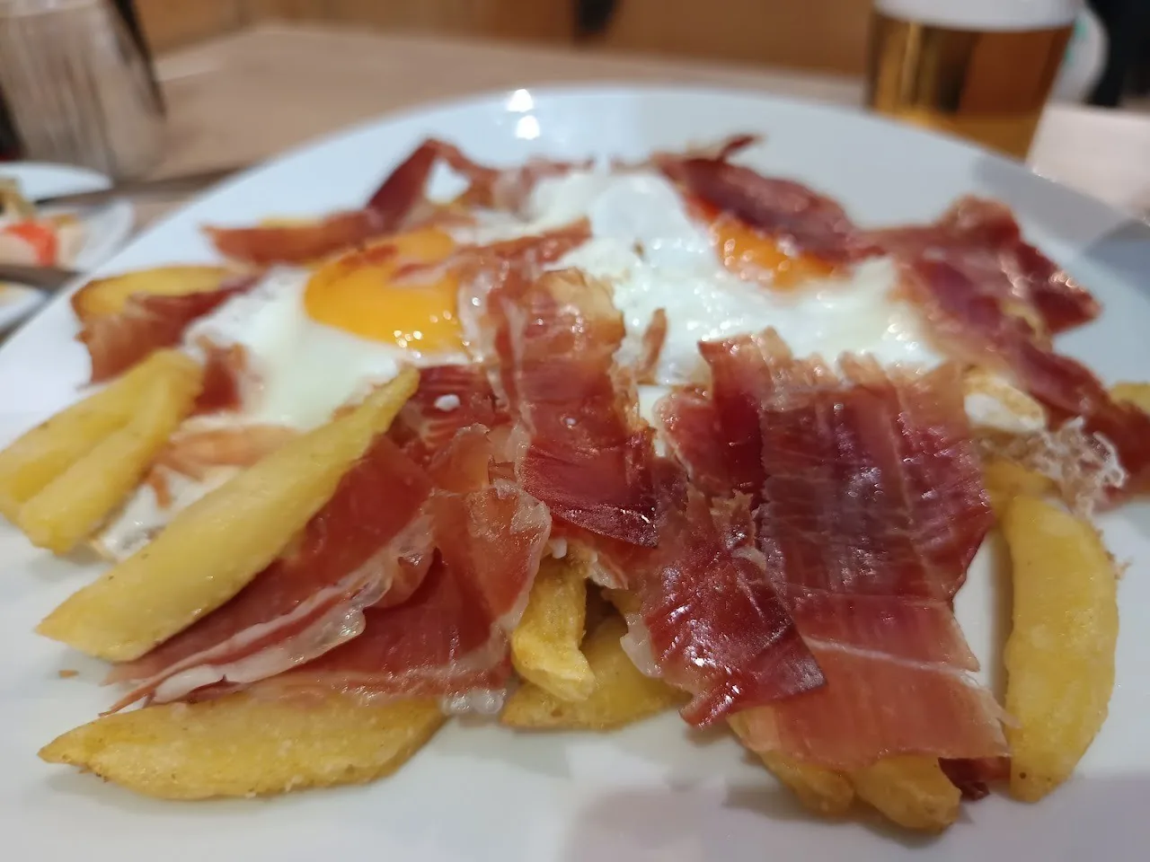 Cured ham and a fried egg over potatoes on a plate