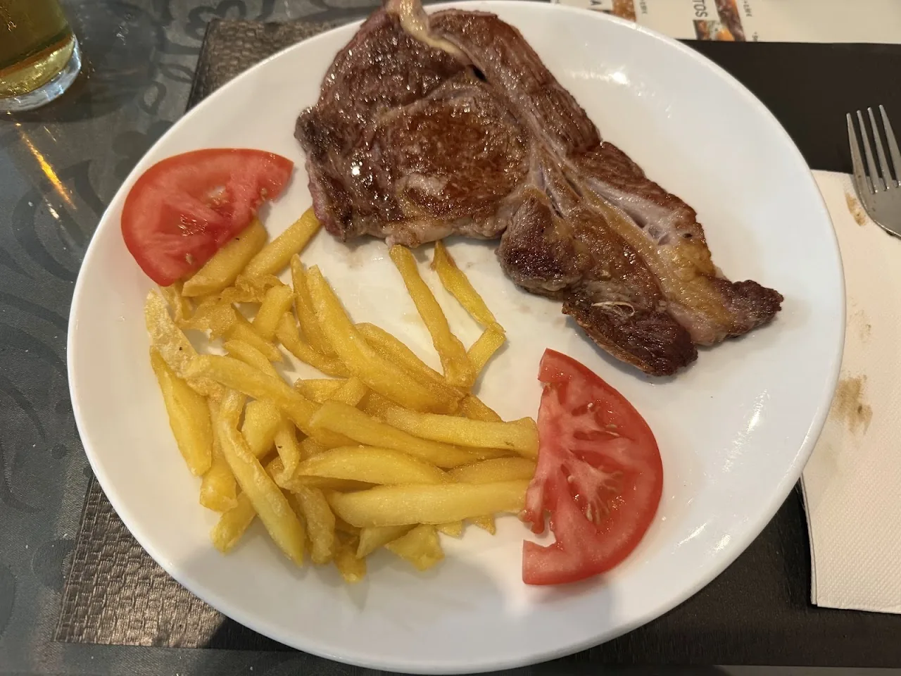A grilled steak with fries and sliced tomato