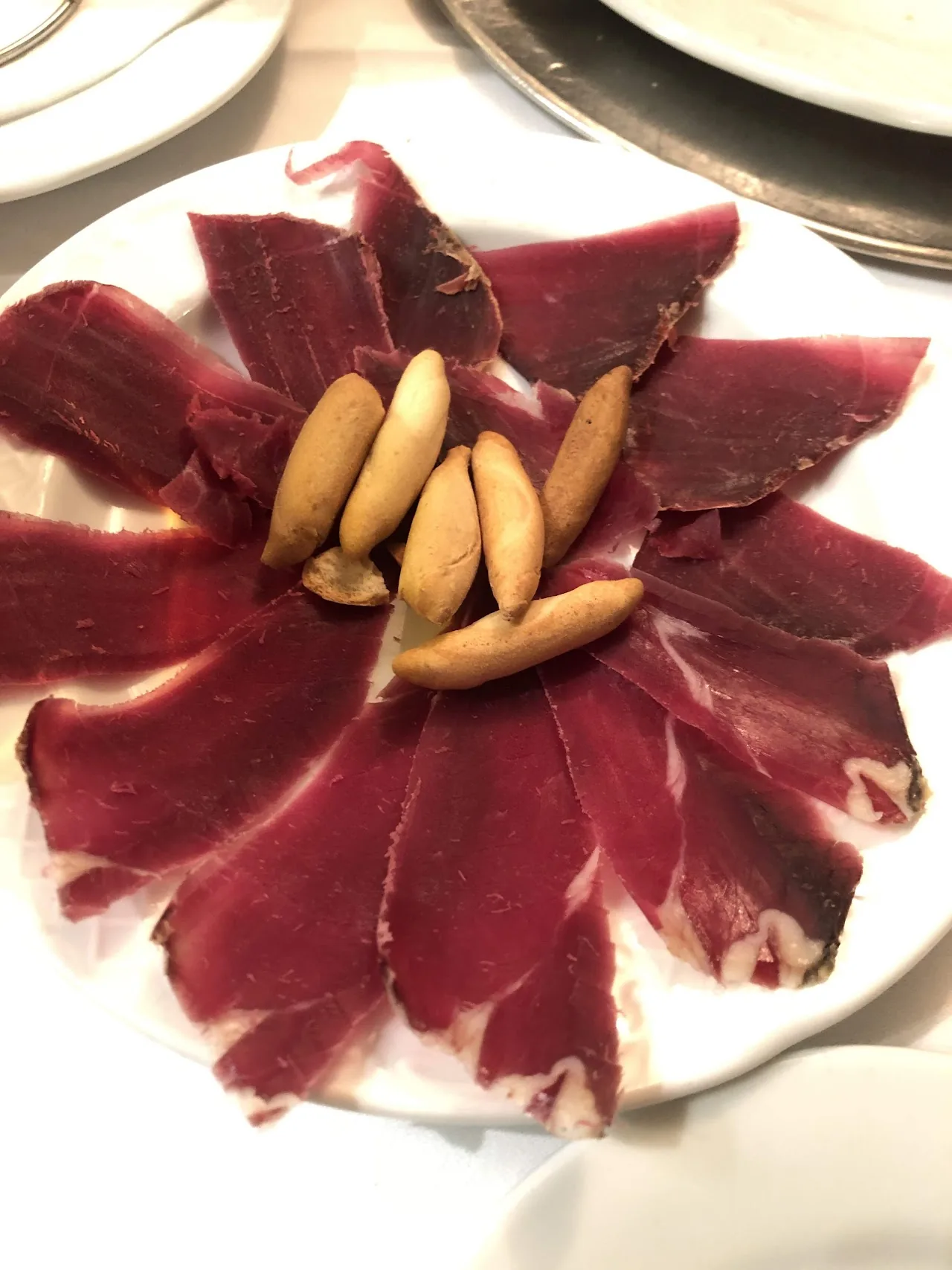 Thinly sliced jamón fanned out with breadsticks arranged in the center