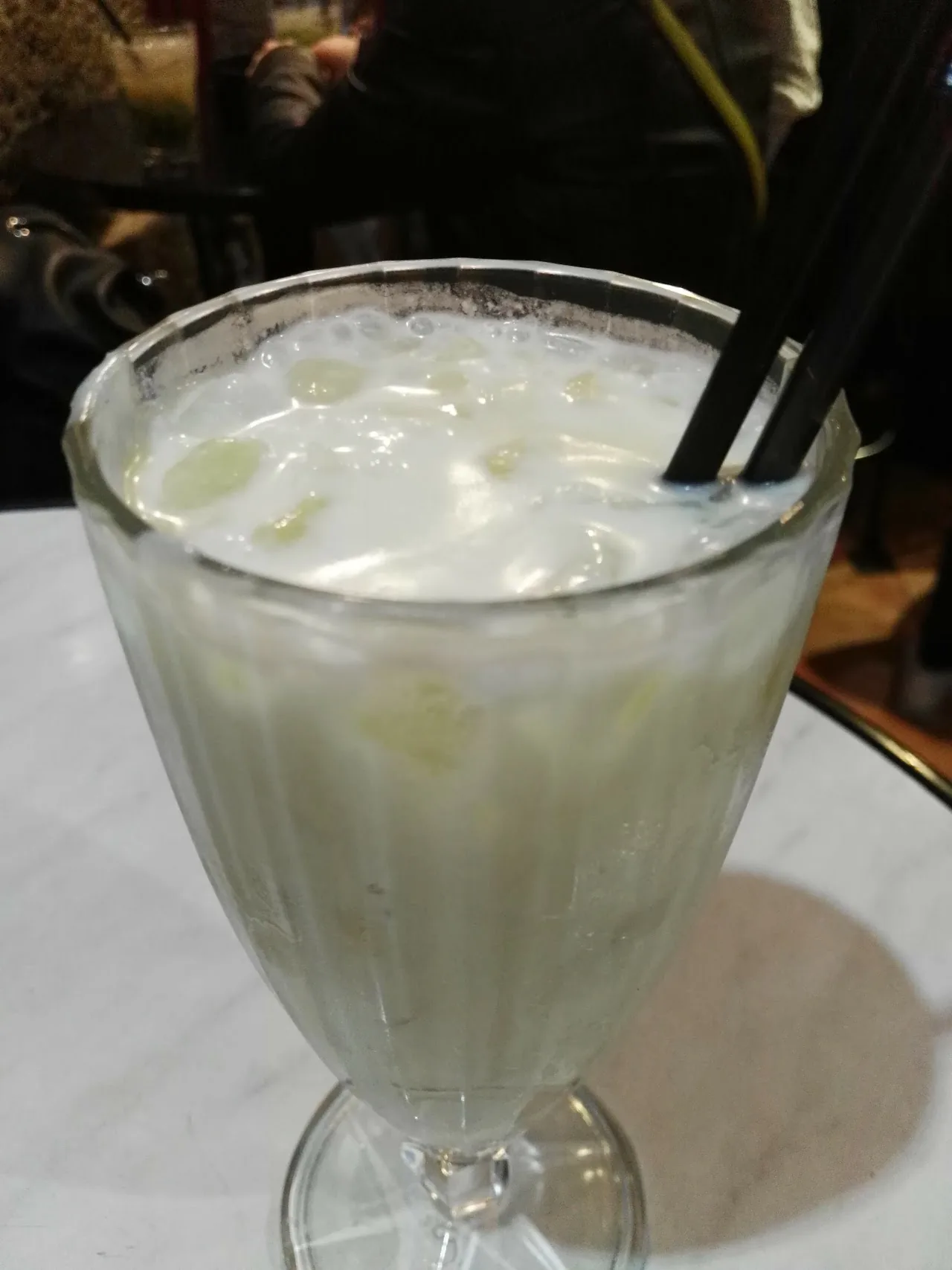 A frothy white cocktail in a stemmed glass with a straw