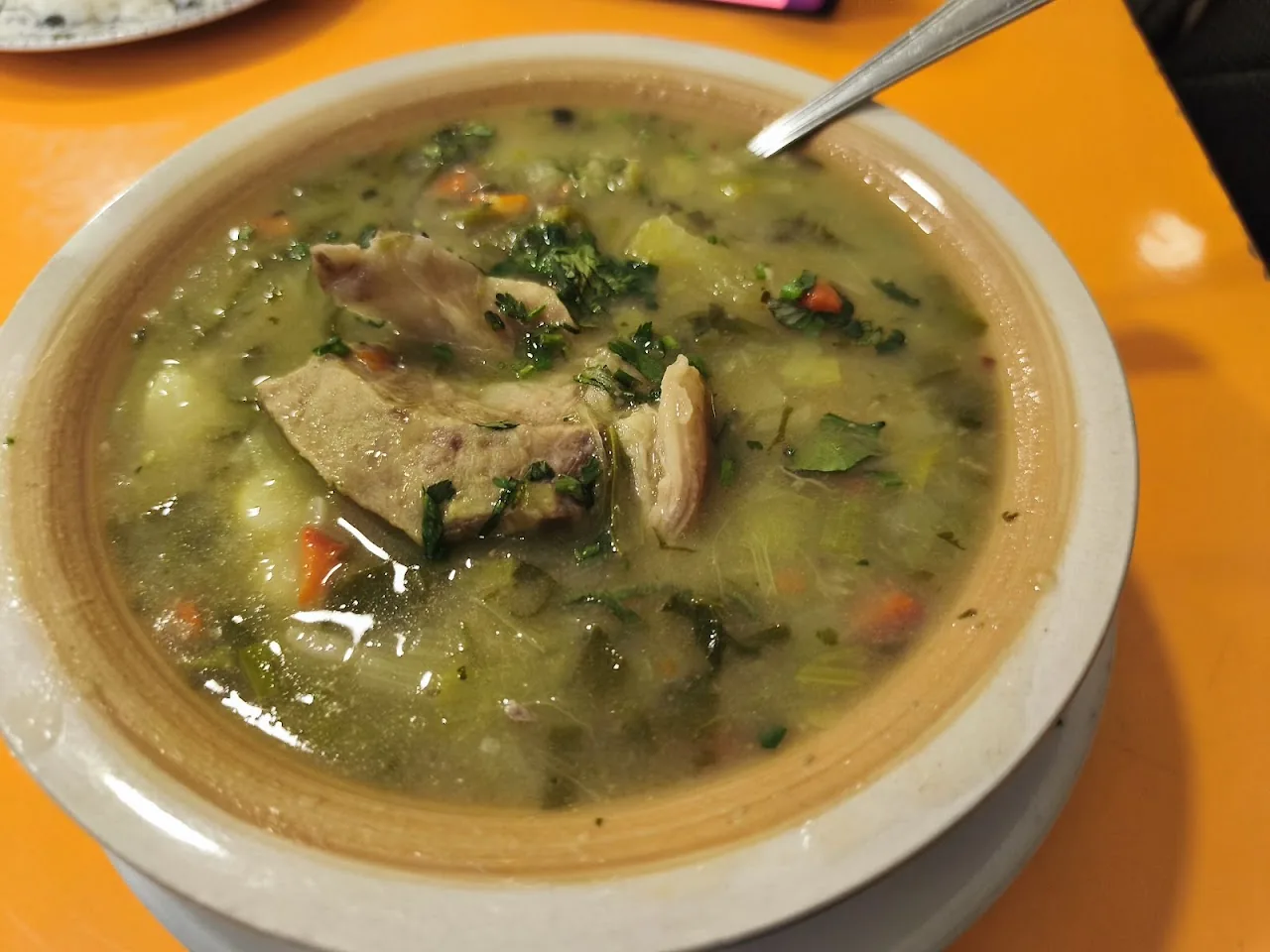 A bowl of green soup with chicken and herbs