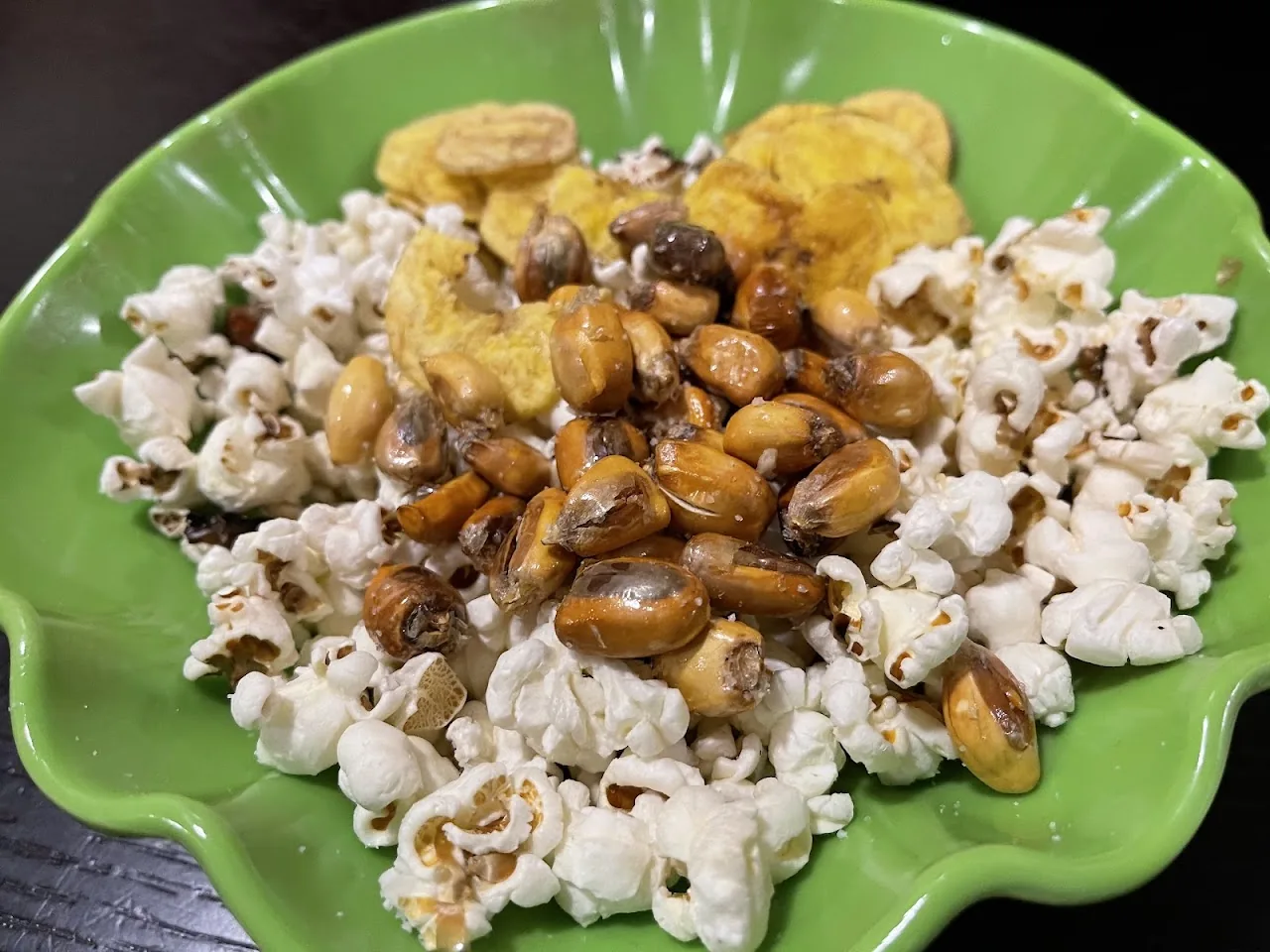 A green plate of popcorn with fried corn nuts and plantain chips