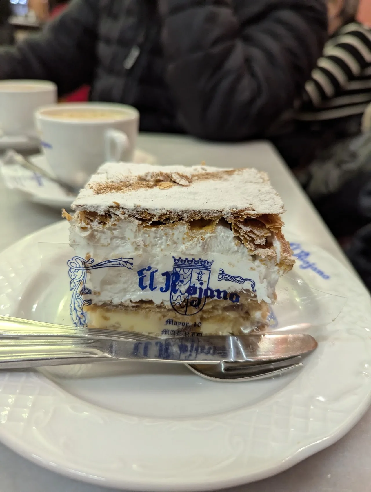 A slice of layered pastry cake on a plate with coffee