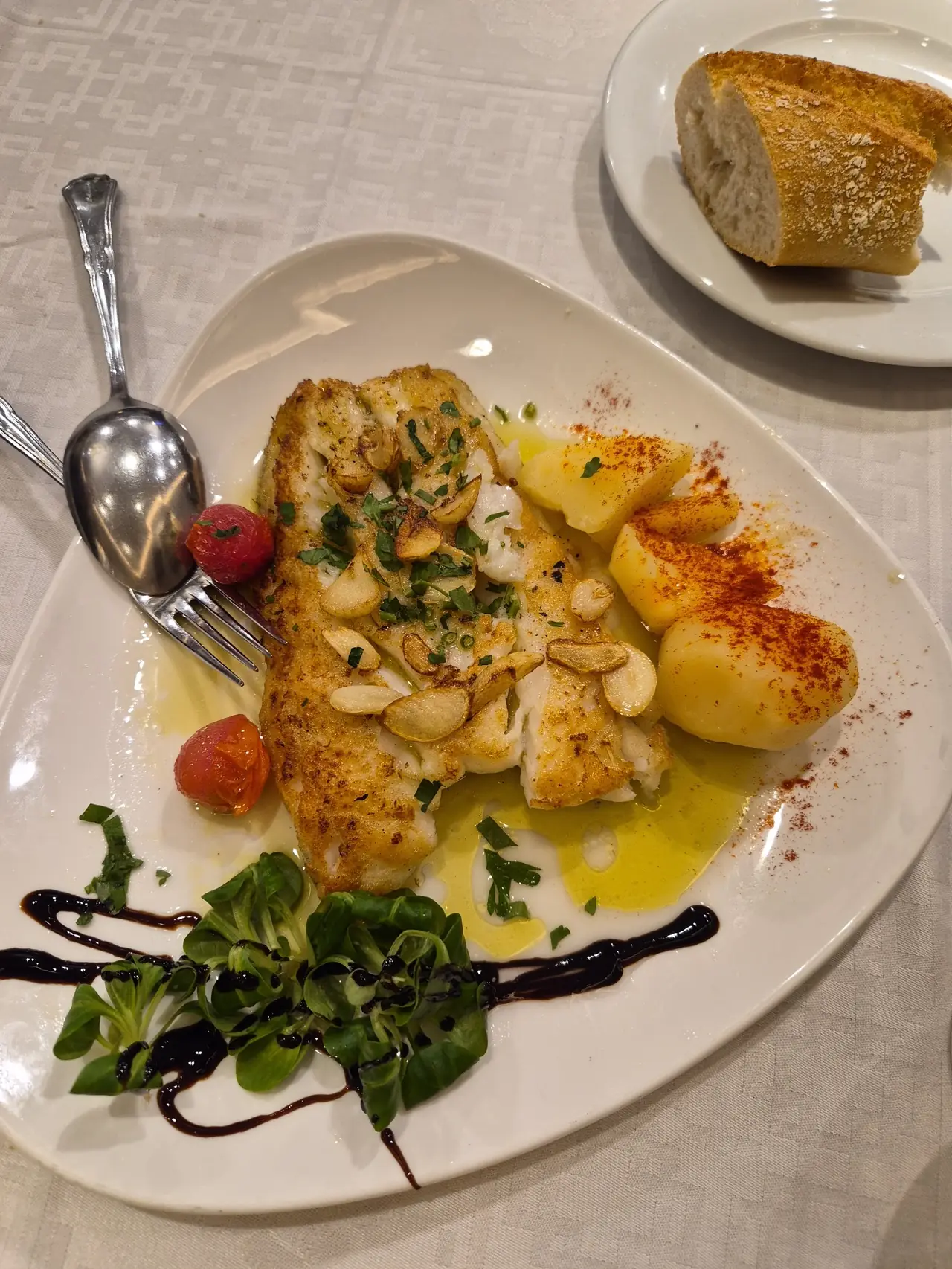 Grilled fish fillet topped with sliced garlic and parsley, served with paprika-dusted potatoes and greens