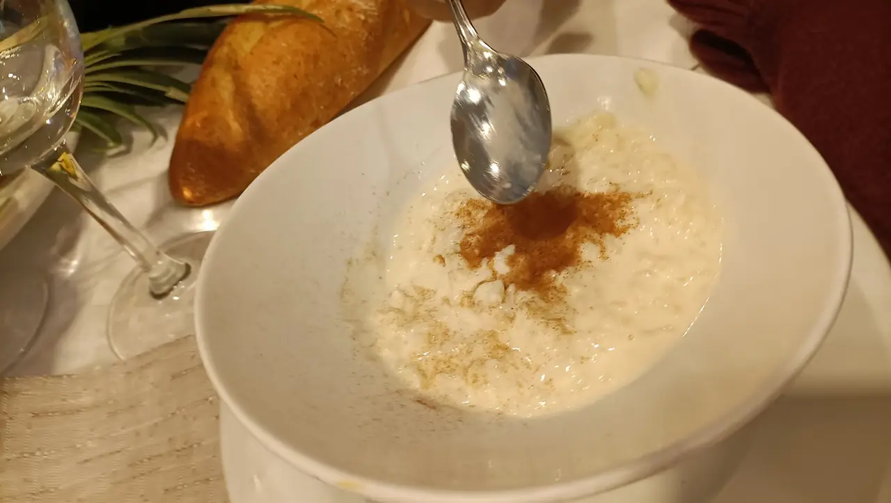 Bowl of rice pudding dusted with cinnamon, a spoon sprinkling more on top