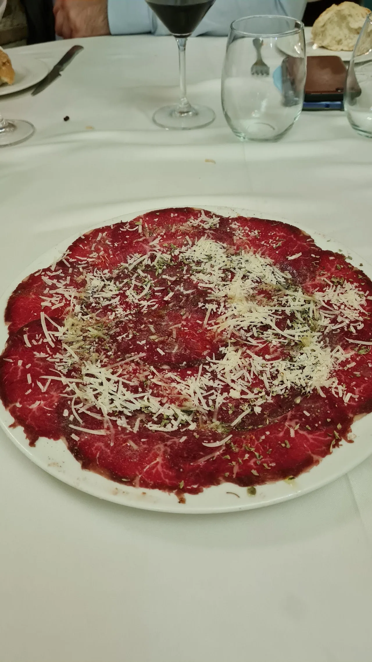 A plate of beef carpaccio topped with grated cheese
