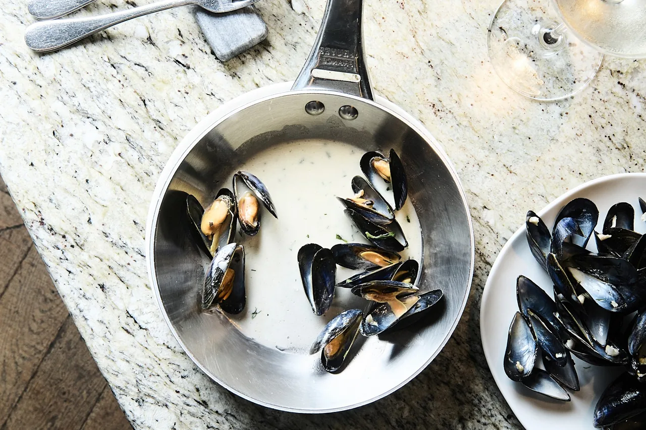 A steel pan of black mussels beside a plate of empty shells