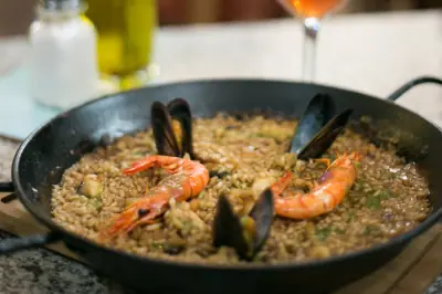 Seafood paella with prawns and mussels in a black pan, served with a glass of rosé wine, at El Sortidor de Filomena Pagès