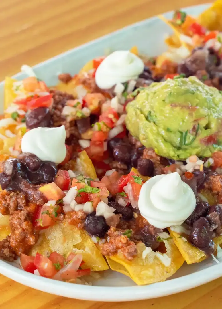 A plate of tortilla chip nachos loaded with ground meat, black beans, pico de gallo, sour cream dollops, and a scoop of guacamole, at El Tianguis
