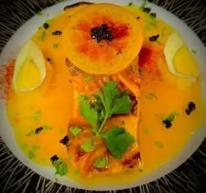 Plated fish in orange sauce with two boiled egg halves, herbs and a torched citrus slice