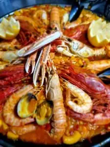Seafood paella loaded with prawns, langoustines, clams and lemon wedges in a pan