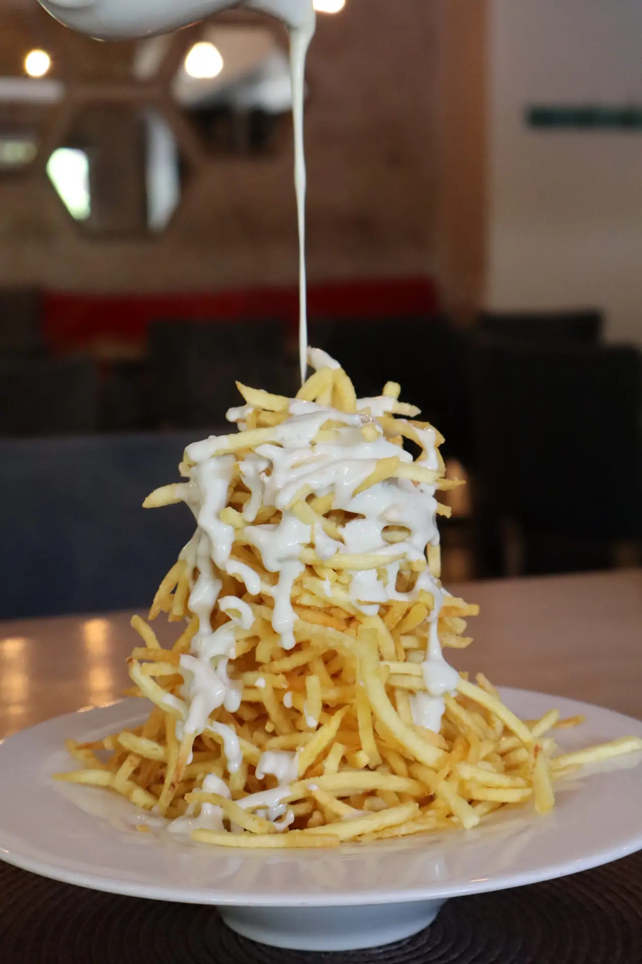 A tall tower of straw potatoes with Cabrales sauce poured over the top, on a white plate