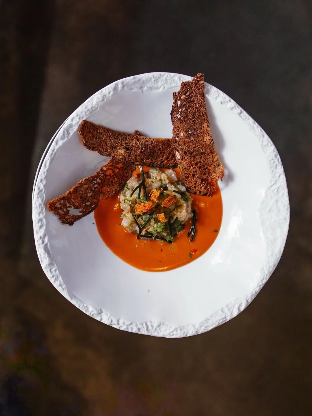 A white bowl with a bright orange sauce topped with a chopped mixture and two slices of dark toast