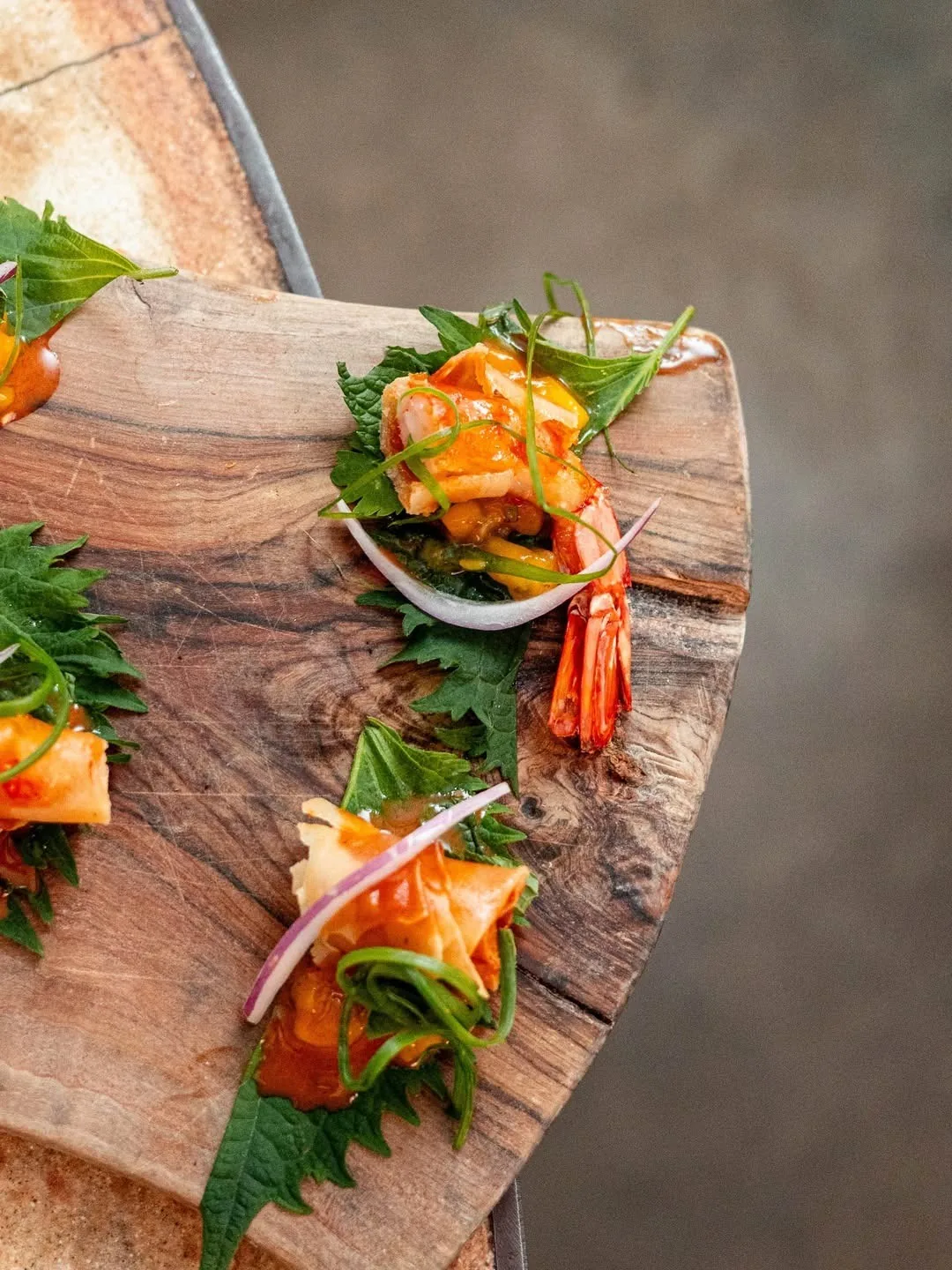 Small portions of orange-topped food with green leaves on a wooden board