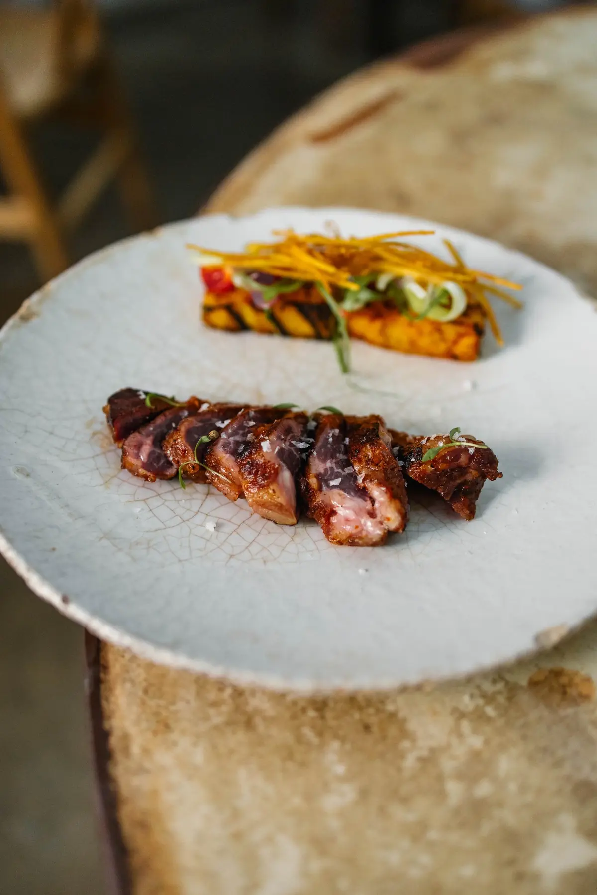 Sliced seared meat with salt flakes next to grilled vegetable strips