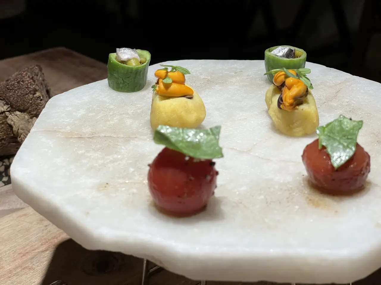 Six small composed bites with mussels, tomato and cucumber on a stone slab