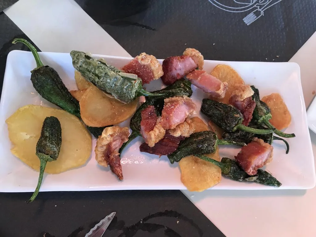 A plate of fried padrón peppers with jamón and orange slices