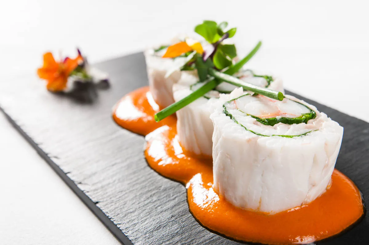 A plated seafood dish with orange sauce and greens
