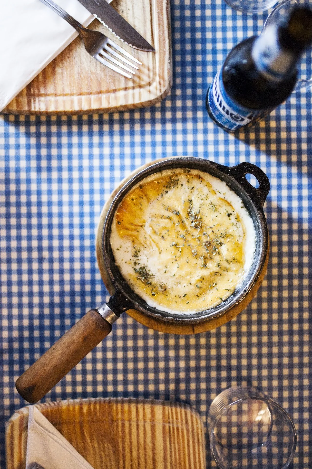 A cast-iron pan of melted cheese sprinkled with herbs on a checked tablecloth