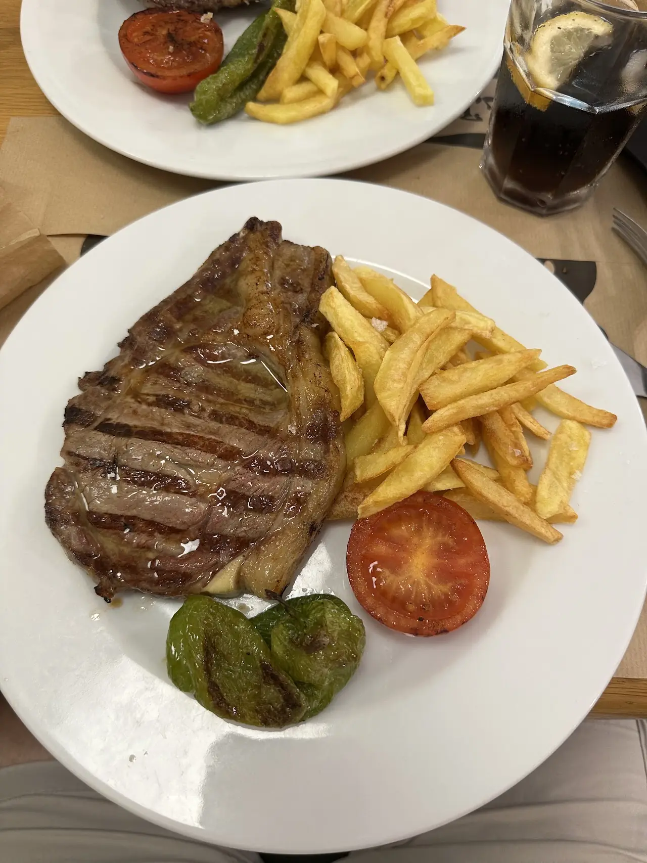 Grilled entrecôte steak with fries, a grilled tomato and a padrón pepper on a white plate, at Elisabets.