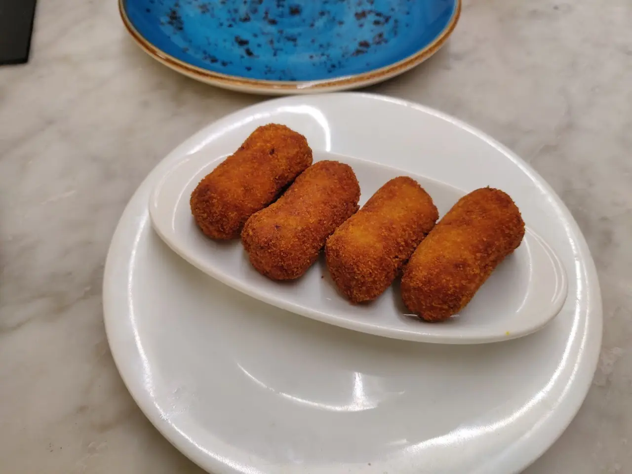 Four breaded croquettes on a white plate, at Elisabets.