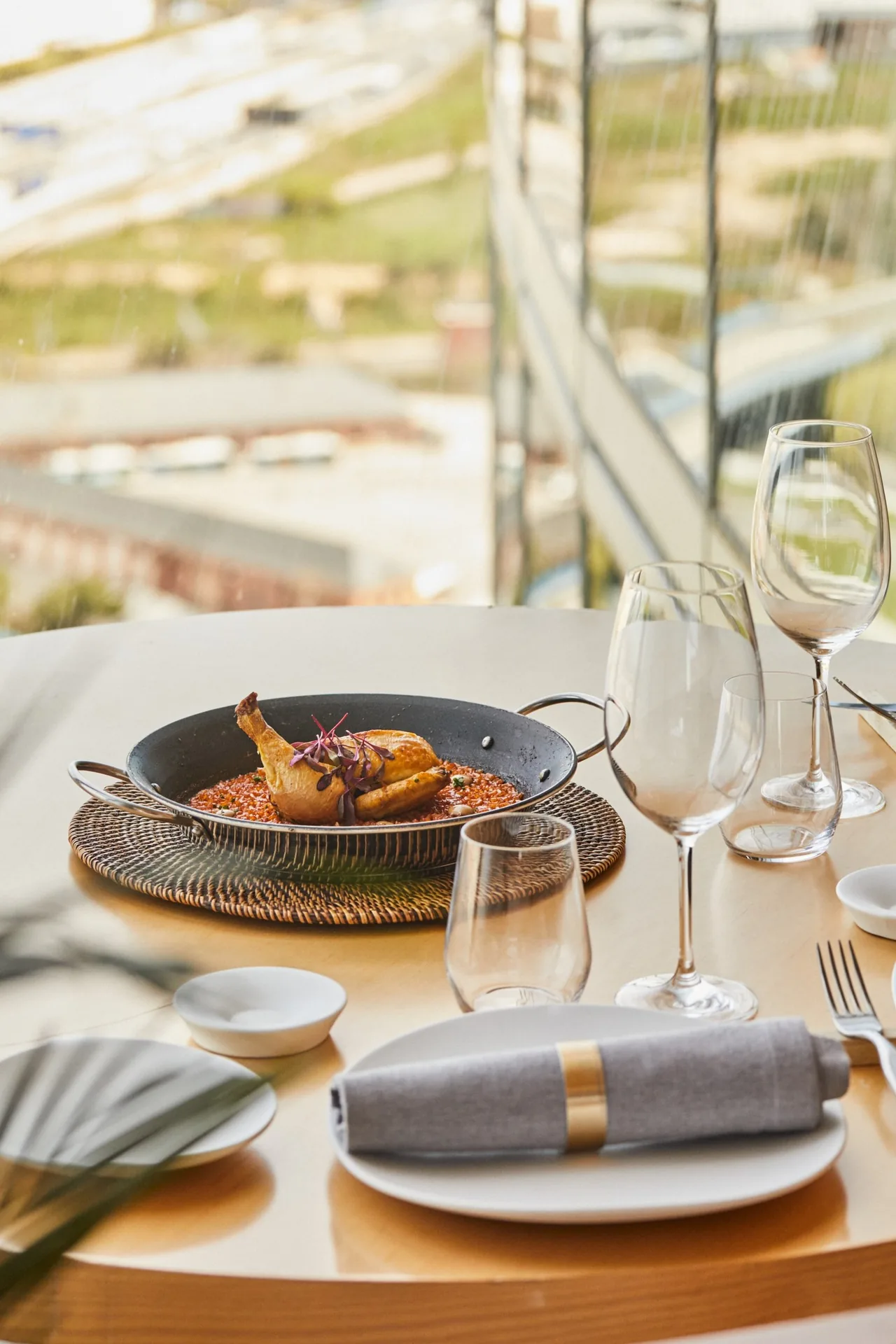 A roast bird in a pan on a set table beside a window with a view over the city