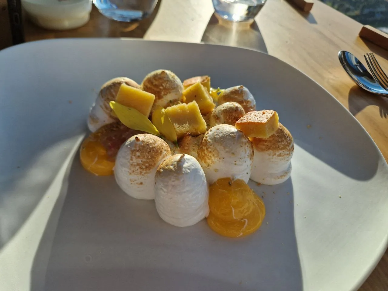 A plated dessert of meringue kisses with mango cubes and cream