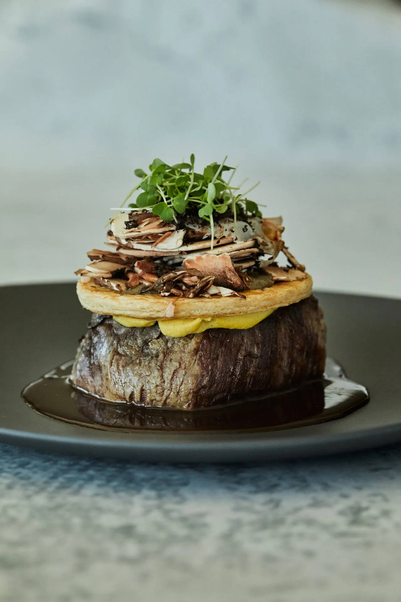 A seared fillet topped with greens on a dark plate