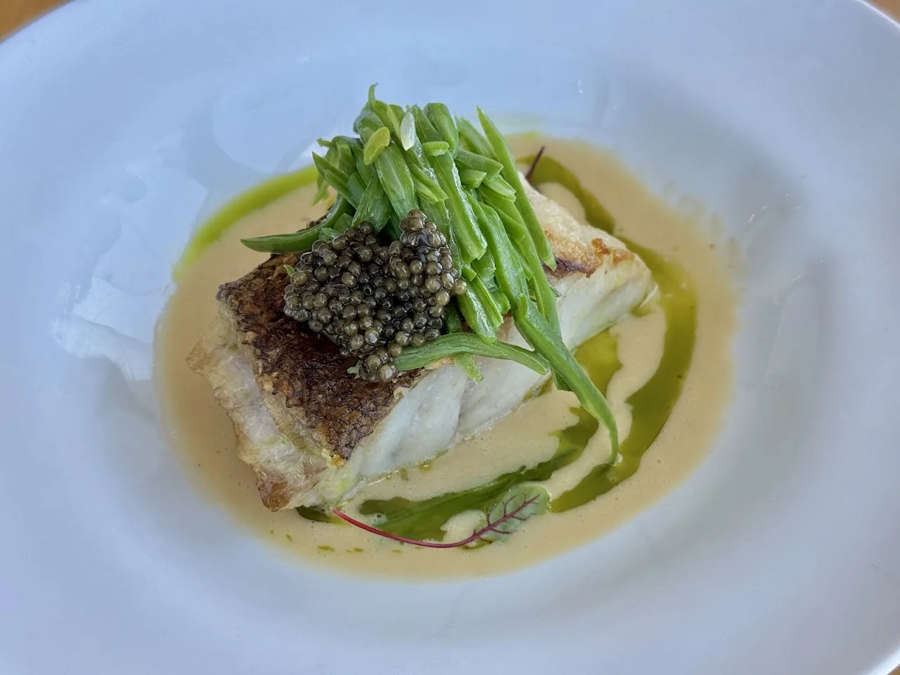 A piece of fish topped with caviar and asparagus in broth