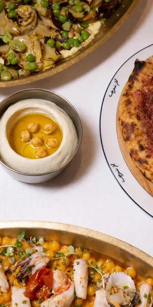 Lebanese spread with hummus topped with chickpeas and olive oil, a charred flatbread on a printed plate and a seafood chickpea dish