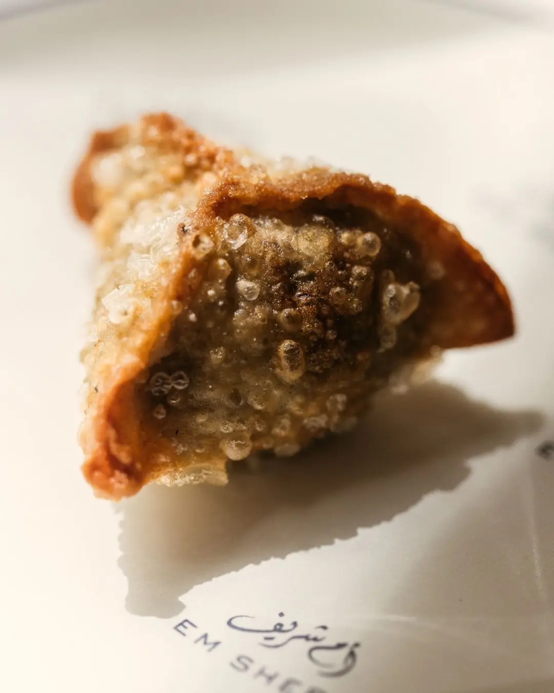 A close-up of a crispy fried pastry on a plate marked with the restaurant's Arabic logo.