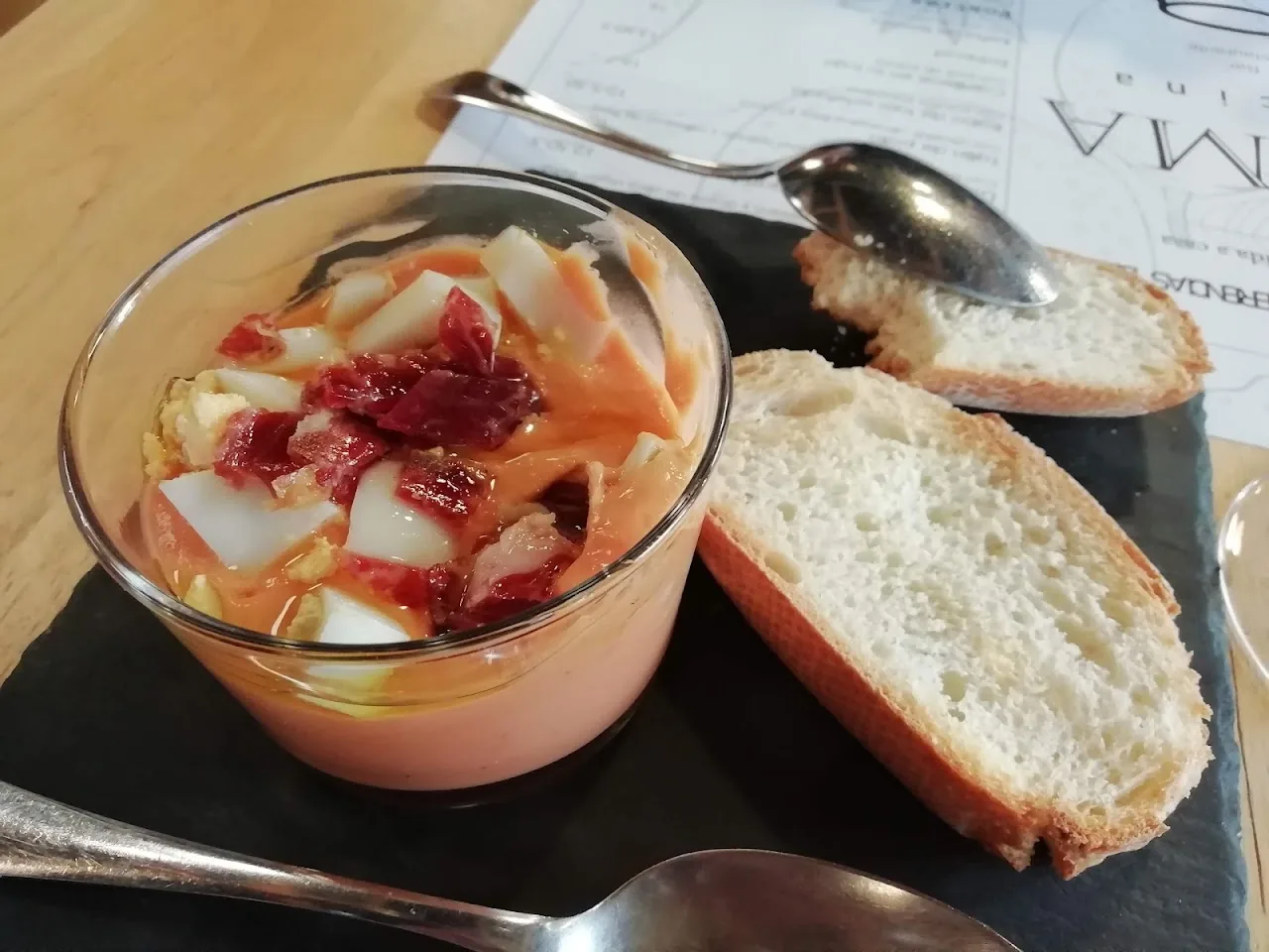 A glass of gazpacho with jamón and crusty bread on the side