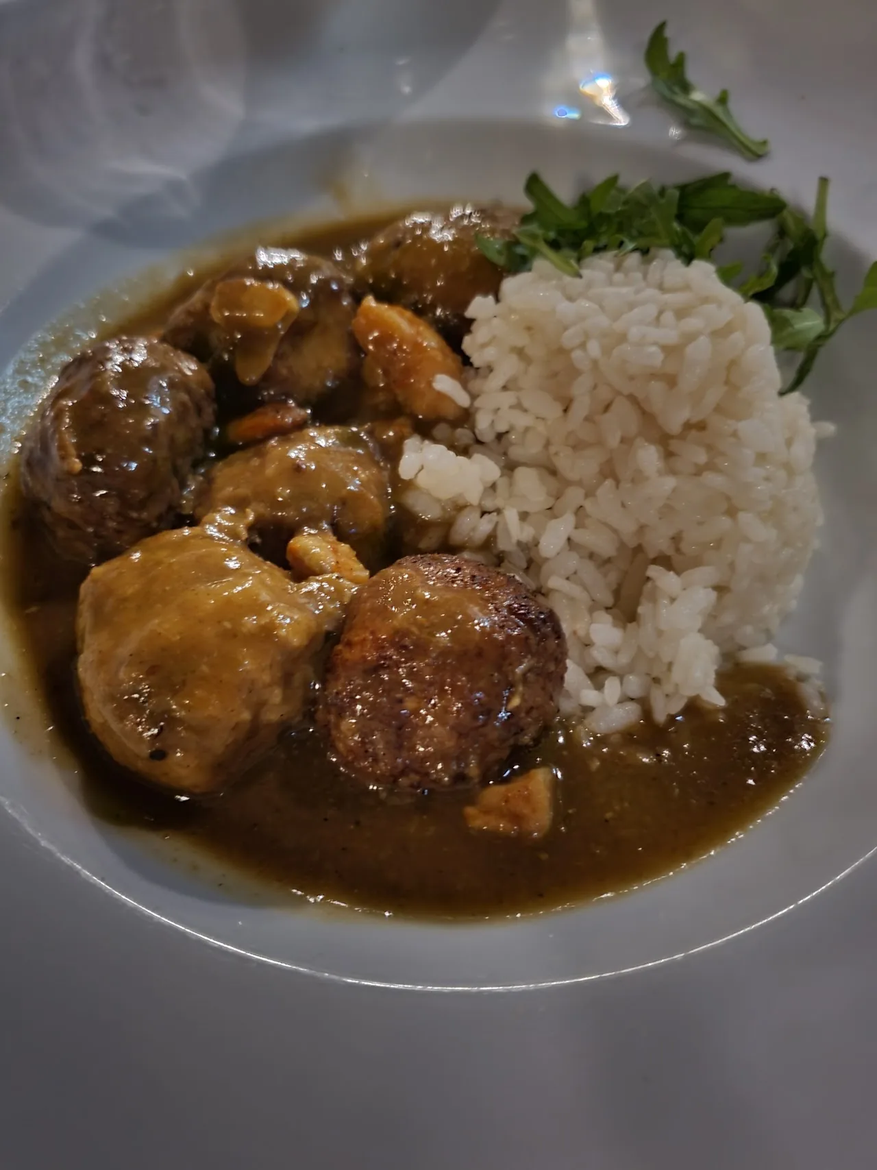 A plate of meatballs in gravy with white rice