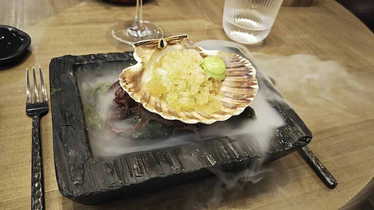 A scallop dish served in its shell wreathed in smoke