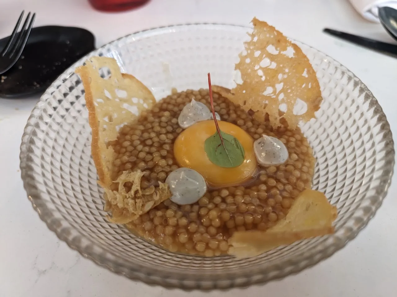 A dessert plate with lentil-shaped beads, a tuile, and a fruit purée swirl