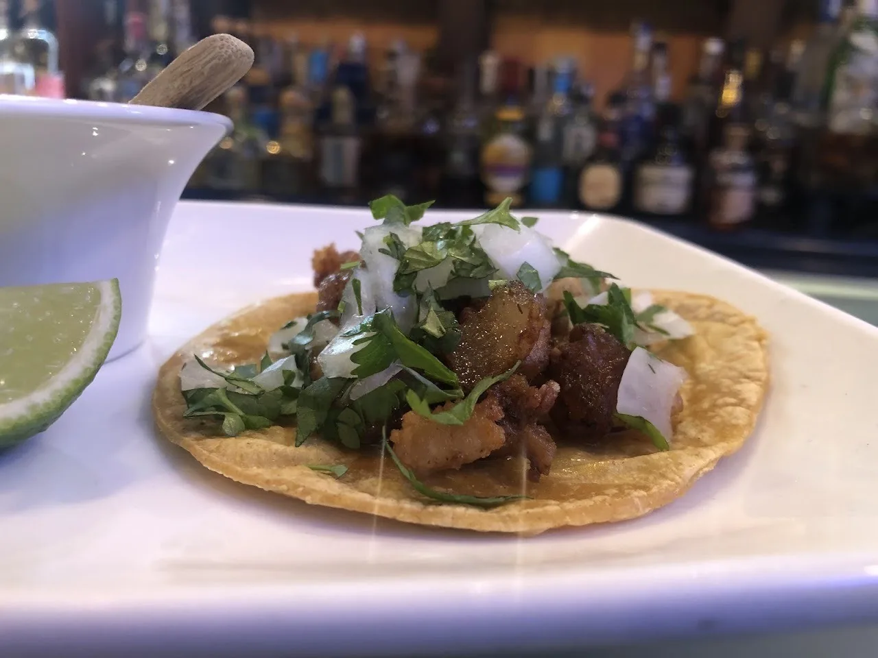A single taco with meat, chopped onion and herbs on a white plate with a lime wedge