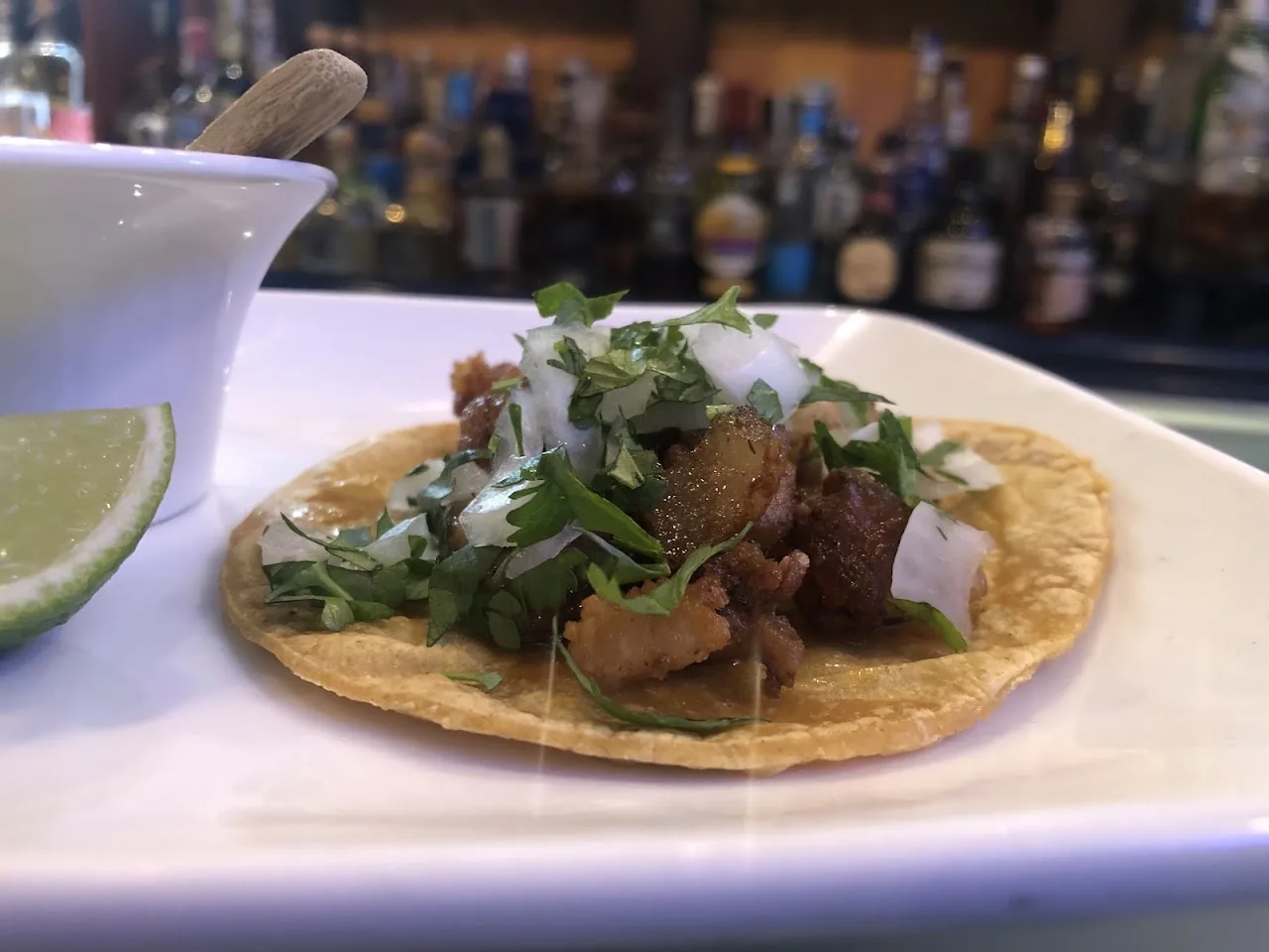 A taco topped with meat, cilantro, and onion next to a lime wedge