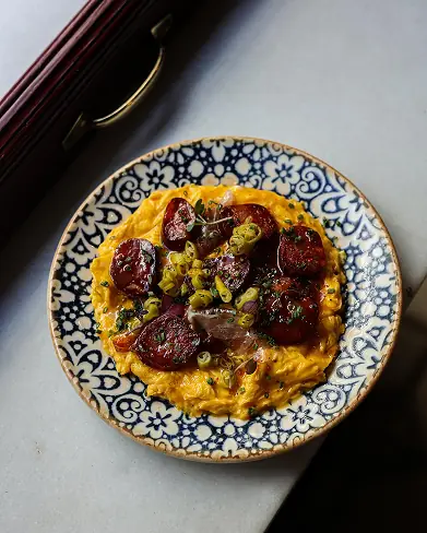 Scrambled eggs topped with sliced chorizo and scallions, served on a blue-and-white patterned plate at Entrepanes Díaz