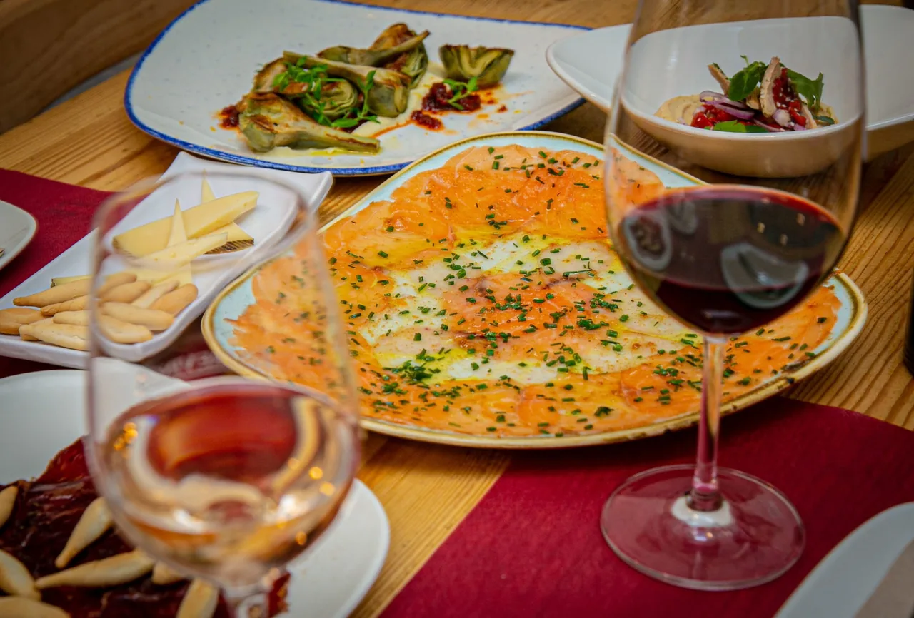 A table with several plates of small dishes and glasses of red and rose wine