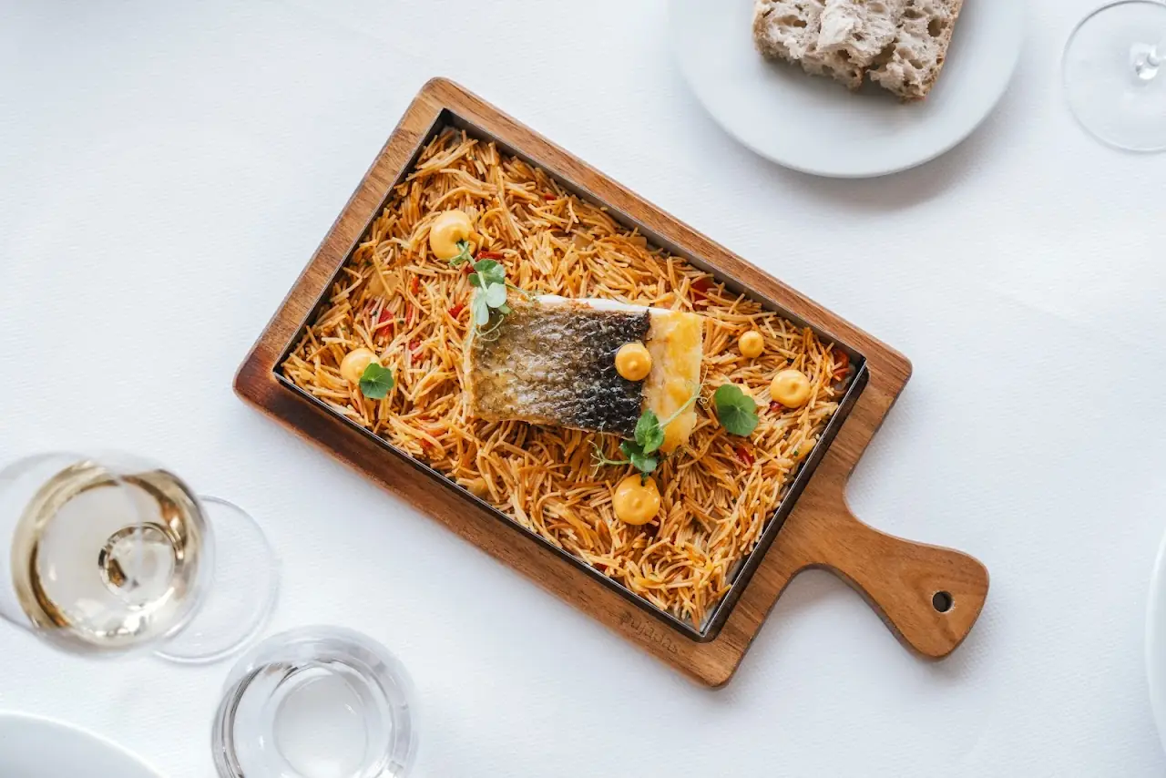 A fish fillet with crispy skin served over toasted noodles on a wooden board.
