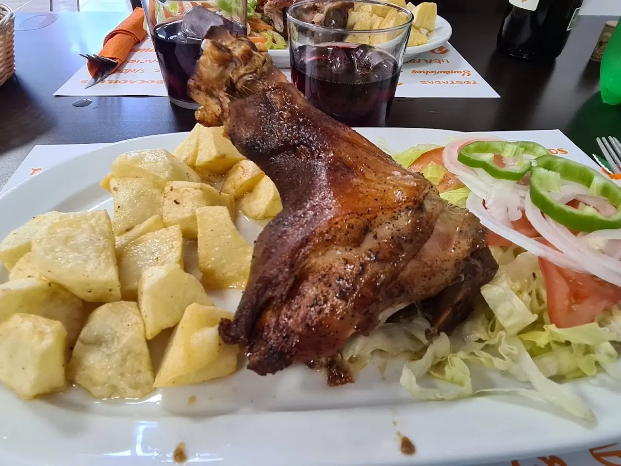 A roasted chicken leg quarter with fried potato wedges, sliced tomato, and onion.