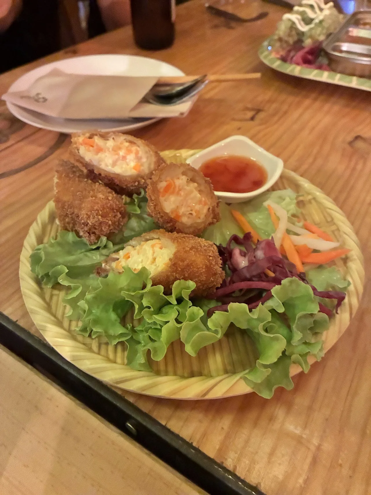 Fried rolls on a bed of lettuce with a small dish of red sauce