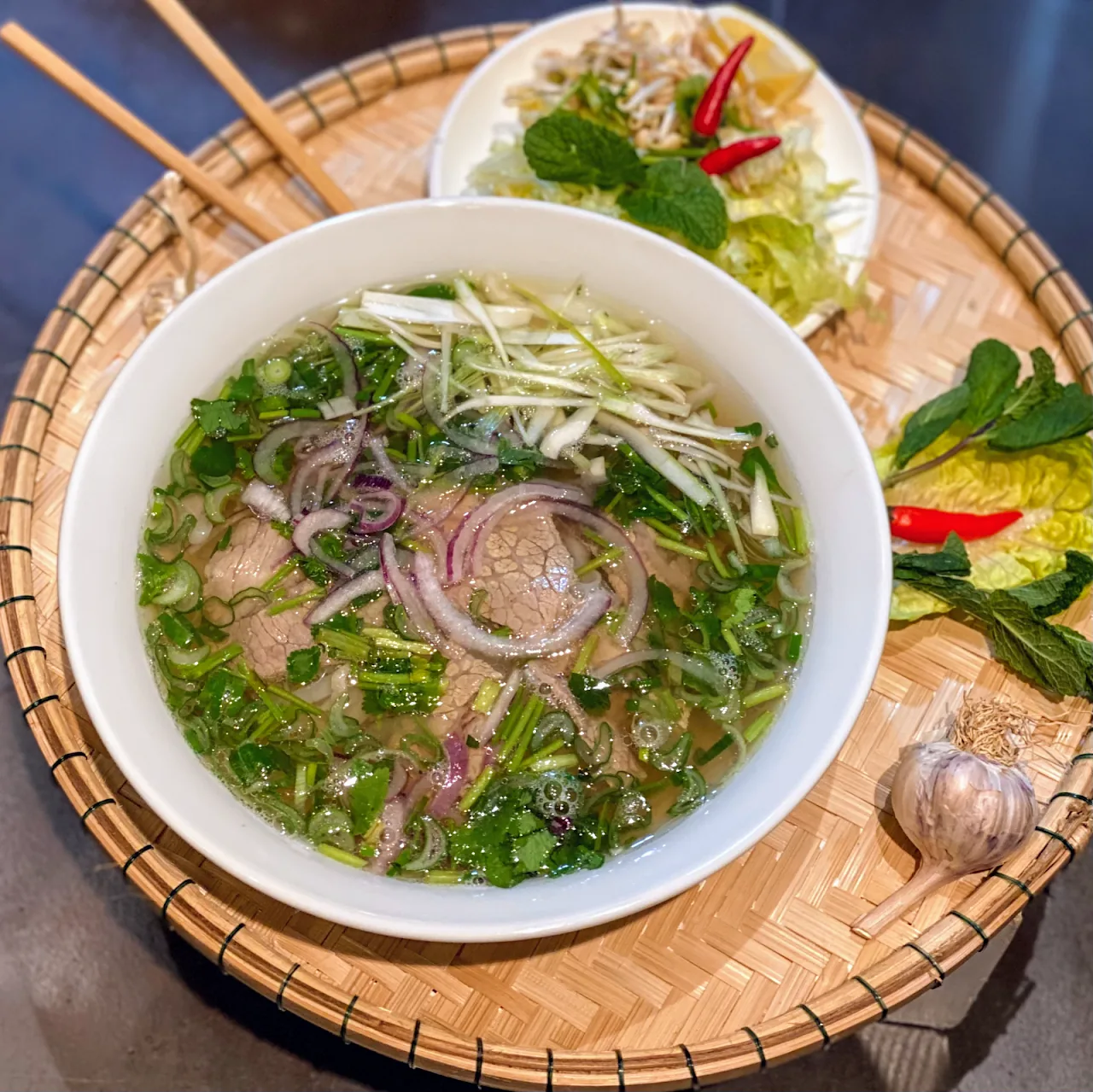 A bowl of pho noodle soup with herbs, onion, and lime